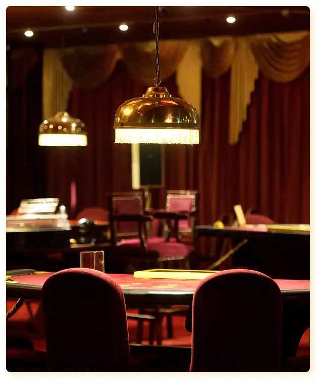Op deze foto is het interieur van een klassieke pokerzaal te zien, badend in zacht, gedempt licht, wat een sfeer van gezelligheid en aristocratische luxe creëert in diepe bordeauxrode tinten.